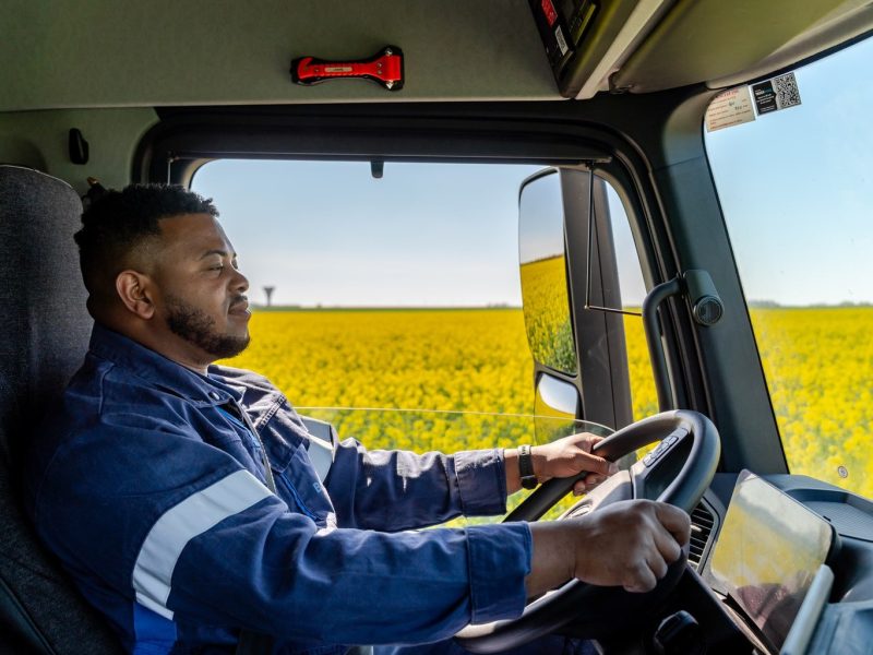 Reportage photo d'entreprise : chauffeur de poids lourd dans sa cabine dans un champ de colza